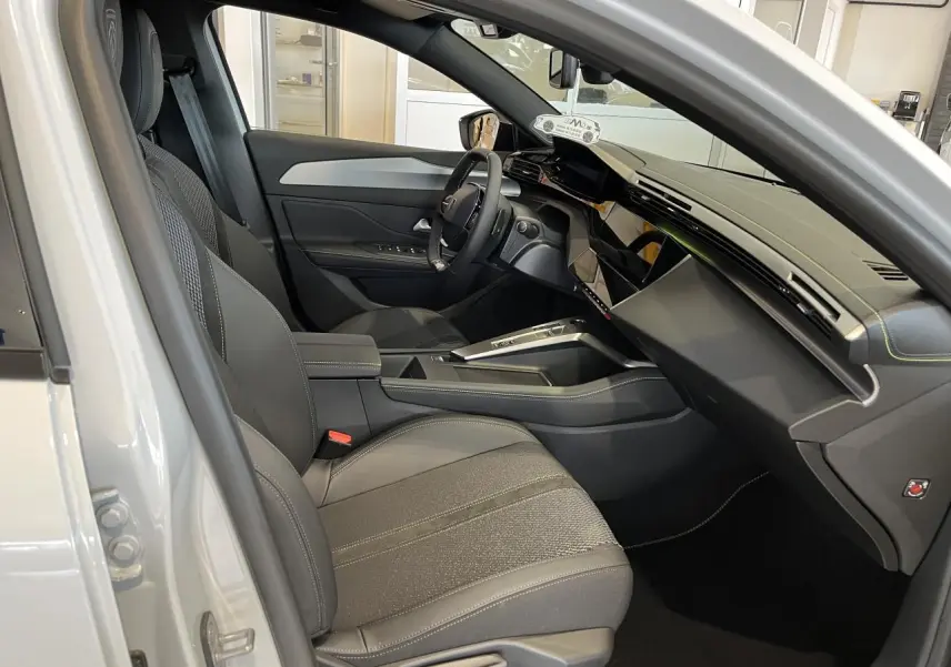Intérieur côté conducteur d'une Peugeot 308 SW blanc okenite, avec tableau de bord moderne et sièges gris tissu et cuir.