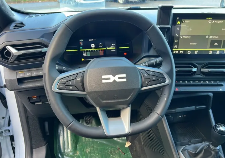 Vue intérieure centrée sur le volant et tableau de bord du Dacia Duster 2025 blanc glacier avec boîte manuelle.