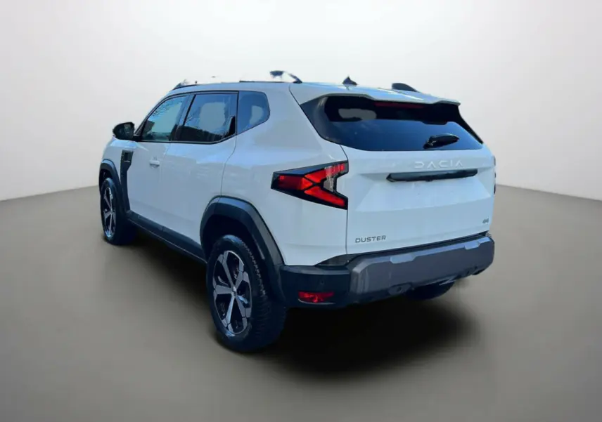 Vue 3/4 arrière du Dacia Duster blanc glacier 2025 avec ses feux arrière en forme de flèche et jantes noires distinctives.