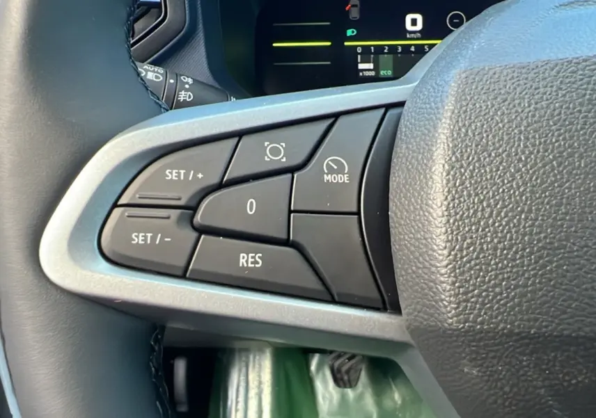 Gros plan sur les commandes au volant côté gauche du Dacia Duster blanc glacier 2025, version NEW TCE 130 4X4 JOURNEY PLUS.