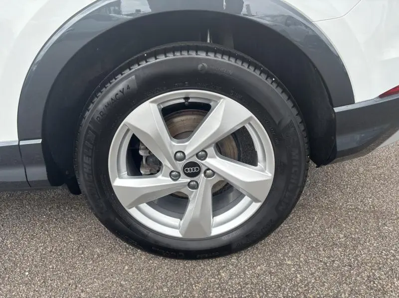 Gros plan sur la roue arrière droite d'un Audi Q3 blanc Glacier métallisé avec jante alu 5 branches et pneu Michelin.