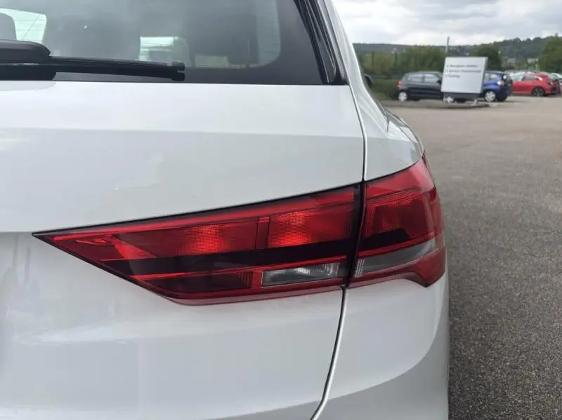 Feu arrière droit rouge du SUV Audi Q3 blanc Glacier métallisé vu en gros plan sur un parking extérieur.
