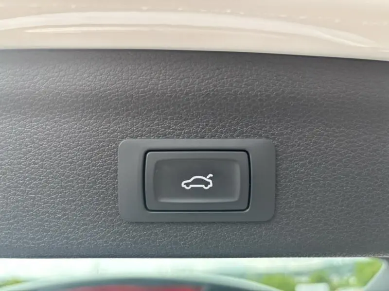 Bouton noir d'ouverture électrique du hayon sur panneau intérieur gris clair d'un Audi Q3 blanc Glacier métallisé.