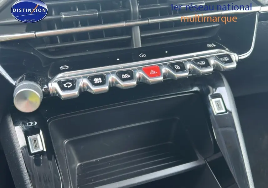 Gros plan sur la console centrale noire brillante de la Peugeot 208 1.2 100 style avec rangements et boutons chromés.