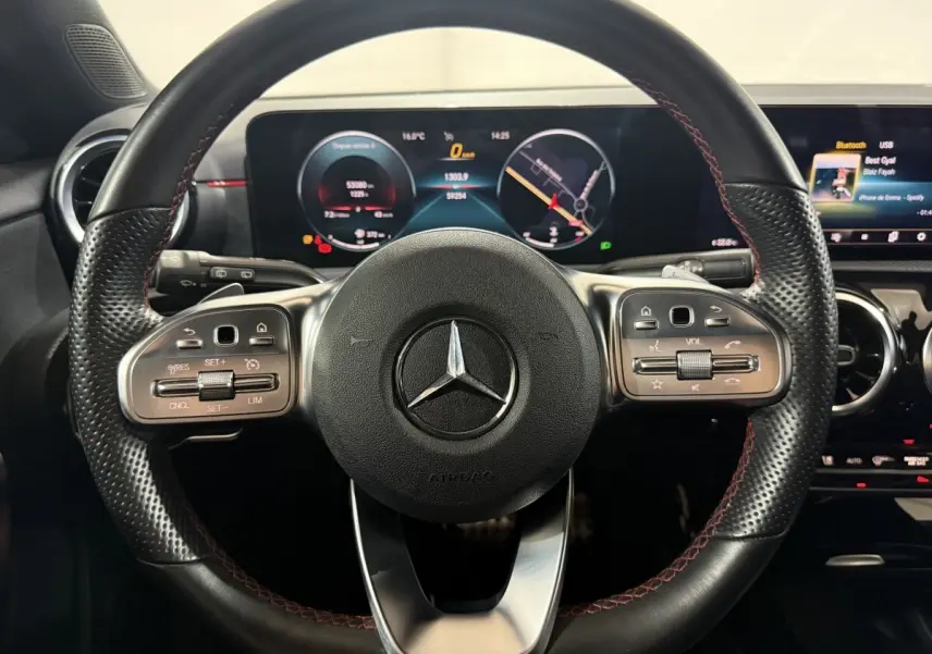 Vue rapprochée du volant cuir noir avec surpiqûres rouges et tableau de bord numérique de la Mercedes Classe A AMG Line 2021.