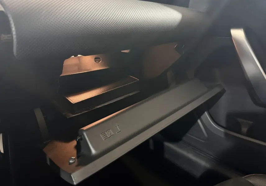 Gros plan de la boîte à gants ouverte du Mercedes Classe A 200 AMG Line 2021, intérieur noir avec éclairage doux.