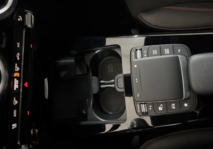 Vue plongeante sur la console centrale noire brillante avec pavé tactile et porte-gobelets d’une Mercedes Classe A gris foncé AMG Line.