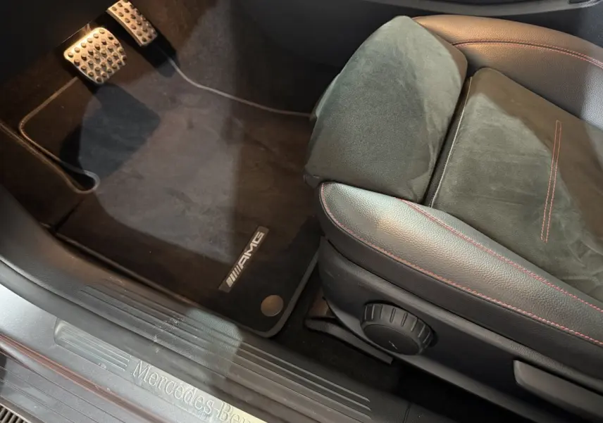 Vue intérieure côté conducteur sur le siège AMG noir avec surpiqûres rouges et seuil de porte Mercedes-Benz gris foncé.