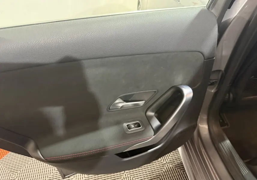 Vue intérieure côté gauche de la porte arrière grise foncée de la Mercedes Classe A 200 AMG Line avec surpiqûres rouges.