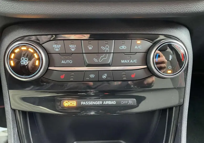 Gros plan sur la console centrale du Ford Puma rouge, montrant les commandes de climatisation et l'indicateur d'airbag passager.