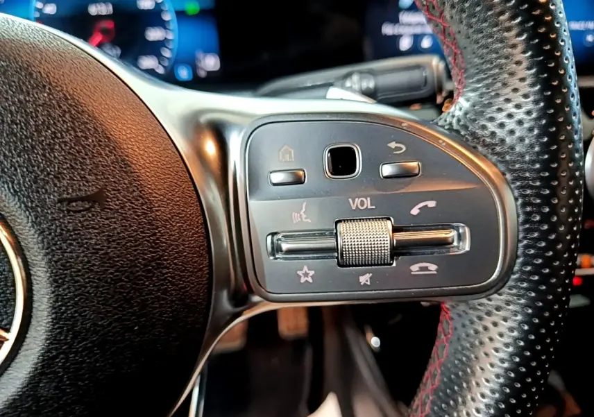 Gros plan sur les commandes de volume et téléphone du volant en cuir noir perforé avec surpiqûres rouges d'une Mercedes Classe A AMG Line 2021.