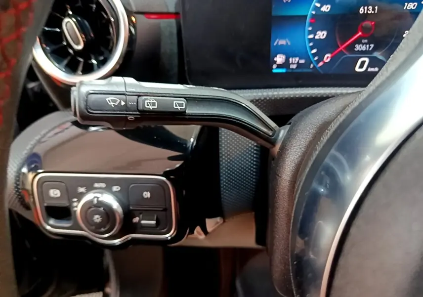 Gros plan sur la commande d’essuie-glace et le tableau de bord numérique bleu d’une Mercedes Classe A 200 AMG Line noire.