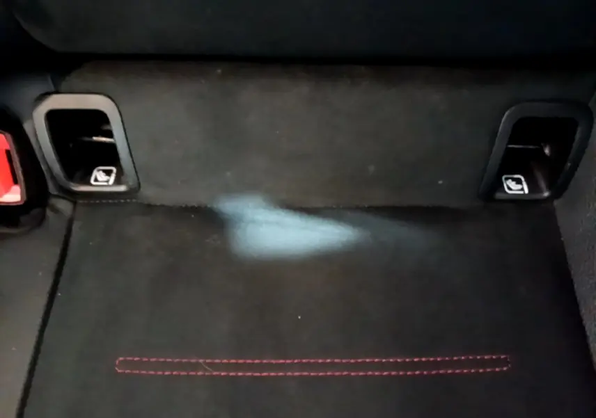 Détail du coffre arrière noir avec fixation Isofix et surpiqûres rouges visibles sur la moquette.