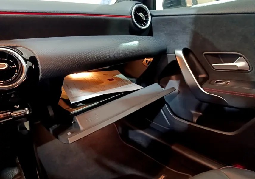 Intérieur noir de la Mercedes Classe A 200 AMG Line 2021, vue côté passager avec boîte à gants ouverte et détails rouges.