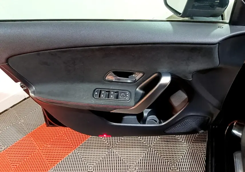 Vue rapprochée de la porte avant gauche noire de la Mercedes Classe A 200 AMG Line avec commandes électriques et surpiqûres rouges.