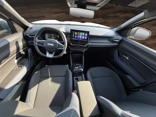 Vue intérieure avant du Dacia Duster Expression Hybrid 140 2025, tableau de bord moderne avec écran tactile central et volant multifonctions cuir synthétique.