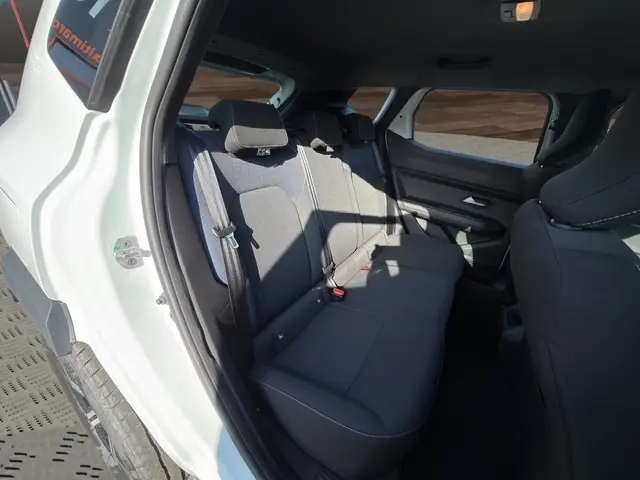 Vue intérieure arrière côté gauche du Dacia Duster blanc 2025, montrant la banquette noire et les appuie-têtes.