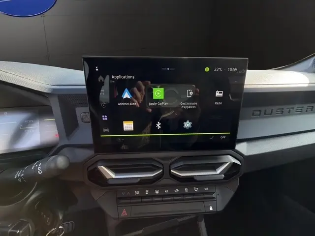 Vue rapprochée de l'écran tactile central du tableau de bord du Dacia Duster blanc 2025, affichant Apple CarPlay et Android Auto.