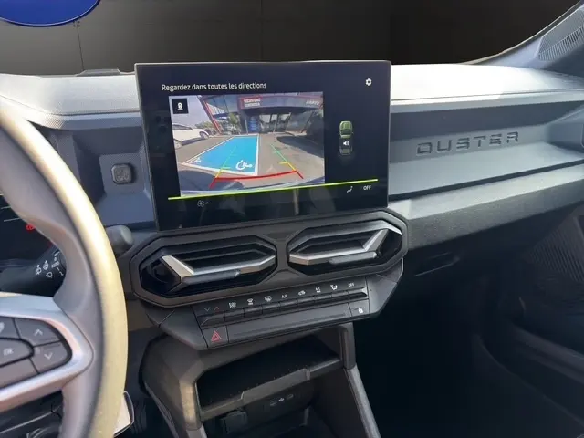 Vue intérieure du tableau de bord du Dacia Duster blanc 2025, écran tactile affichant la caméra de recul avec guidage.
