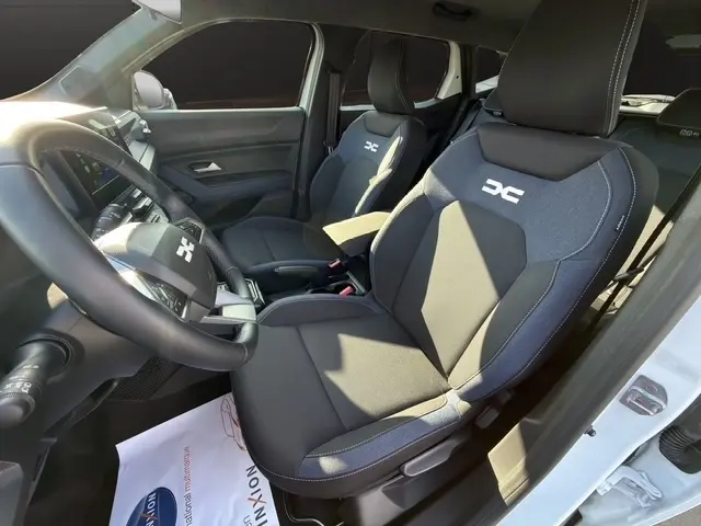 Vue intérieure côté conducteur du Dacia Duster Expression Hybrid 140 blanc, sièges tissu avec logo DC brodé.