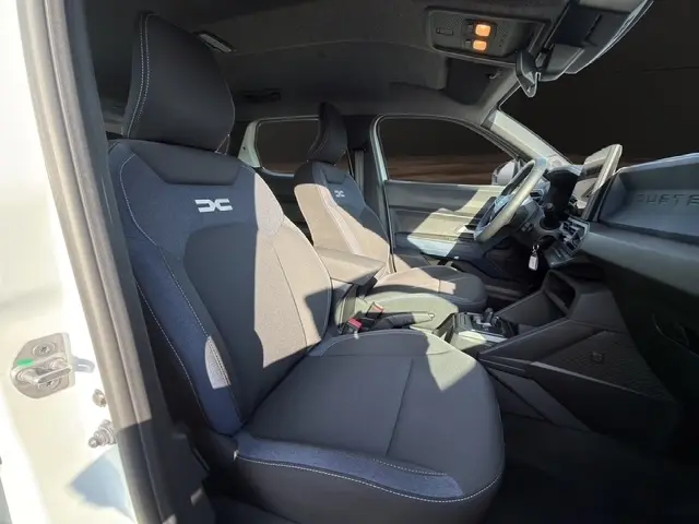 Intérieur du Dacia Duster Expression Hybrid 140 blanc, vue côté gauche sur les sièges avant et tableau de bord moderne.