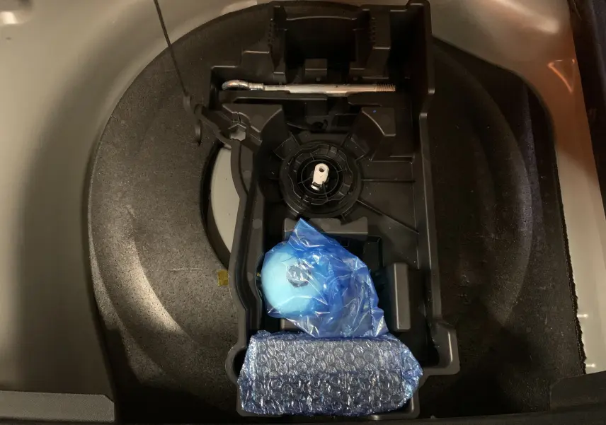 Vue plongeante sur le compartiment de rangement sous le coffre du DS7 Crossback gris Platinium, avec outils emballés visibles.