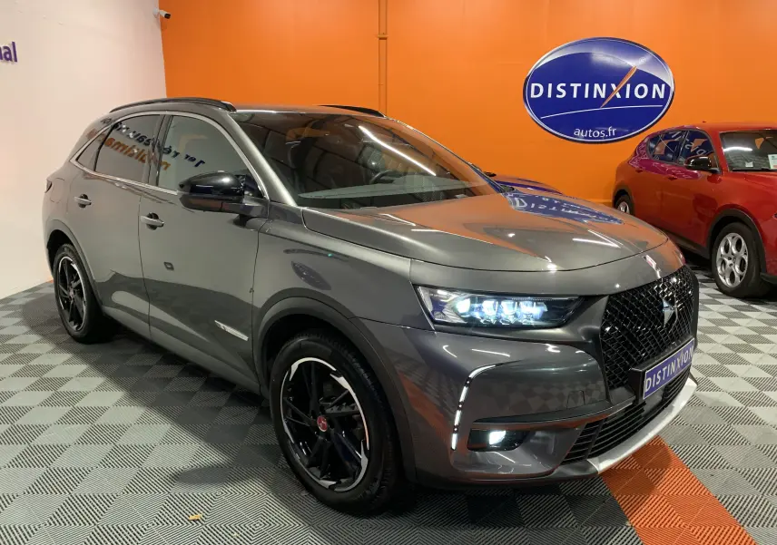 DS7 Crossback gris Platinium en 3/4 avant droit, phares LED allumés et jantes noires distinctives dans un showroom.