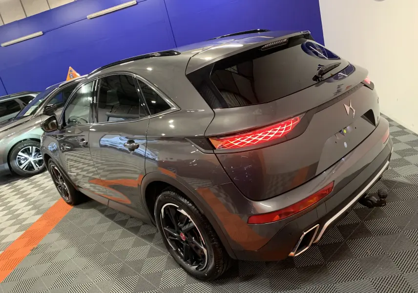 Vue 3/4 arrière droite du DS7 Crossback gris Platinium avec feux arrière allumés et jantes noires brillantes.