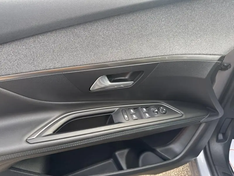 Intérieur côté gauche de la porte avant gris Artense du Peugeot 3008 2022, avec commandes électriques et poignée chromée.