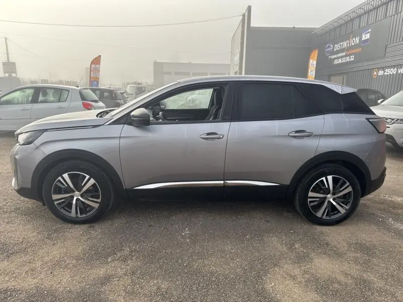 Profil latéral gauche d'un Peugeot 3008 gris Artense avec jantes alliage et vitres arrière surteintées sur parking extérieur brumeux.