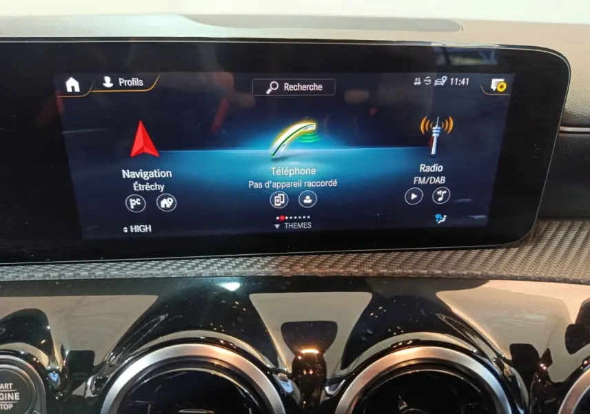 Vue rapprochée de l’écran tactile central et des aérateurs ronds noirs du tableau de bord d’une Mercedes Classe A bleu.