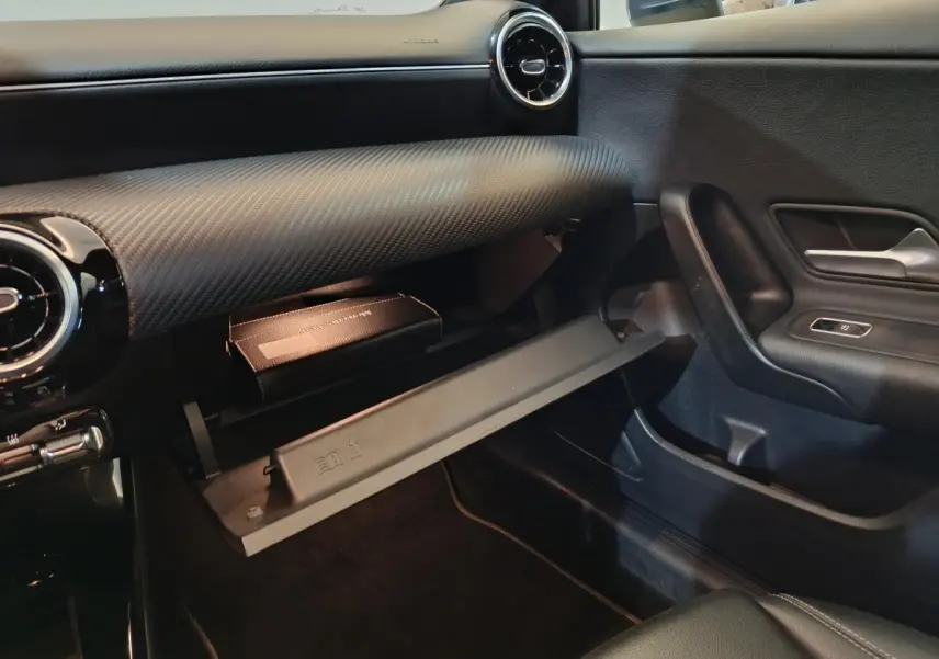 Intérieur côté passager de la Mercedes Classe A 250 e bleu, boîte à gants ouverte avec manuel visible, tableau de bord noir.