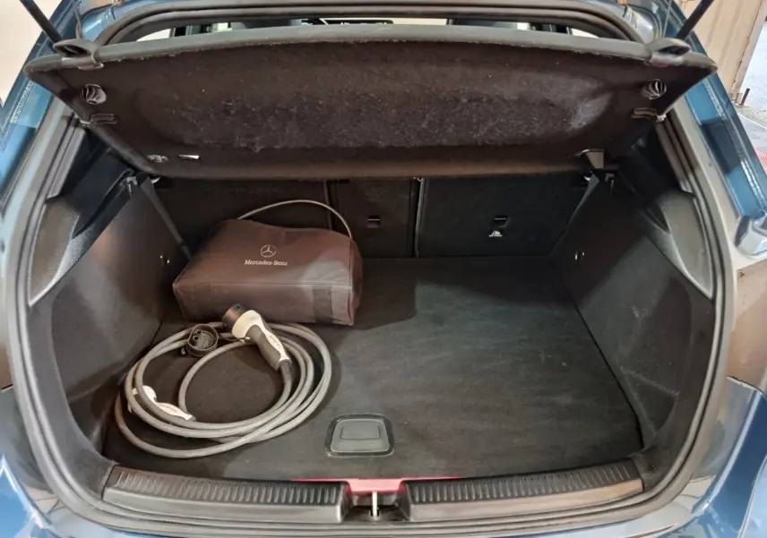 Coffre ouvert d'une Mercedes Classe A 250 e Business Line bleu, avec câble de recharge et sac de rangement Mercedes.