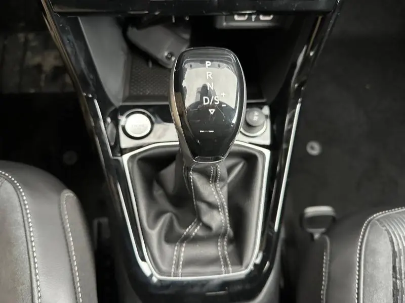 Vue rapprochée du levier de vitesses automatique noir du Volkswagen T-Cross 1.0 TSI R-Line, entouré de garnitures brillantes.