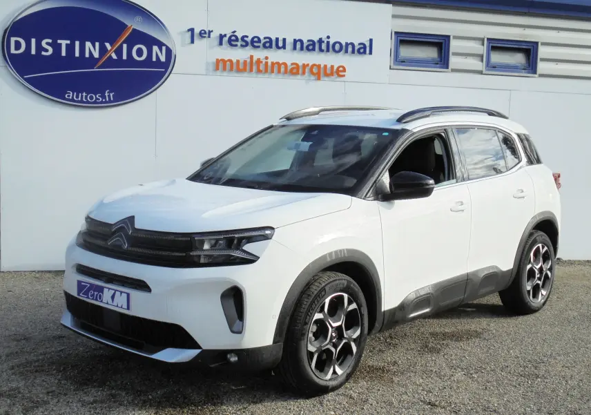 Citroën C5 Aircross blanc banquise en 3/4 avant droit avec jantes biton et barres de toit noires.
