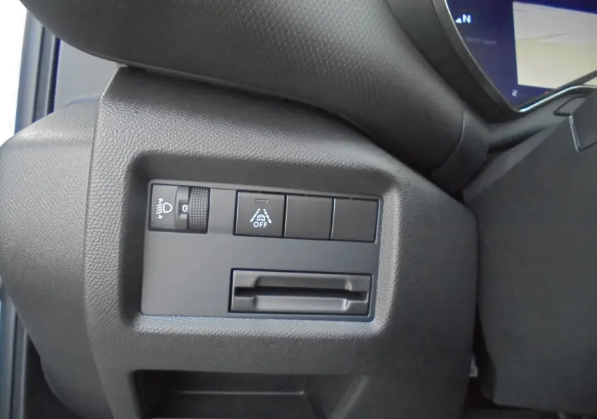 Gros plan sur les commandes de réglage des phares et d'aide à la conduite du tableau de bord noir d'une Citroën C5 Aircross blanche.