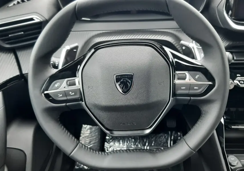 Vue rapprochée du volant cuir noir du Peugeot 2008 2025, avec commandes intégrées et tableau de bord numérique.