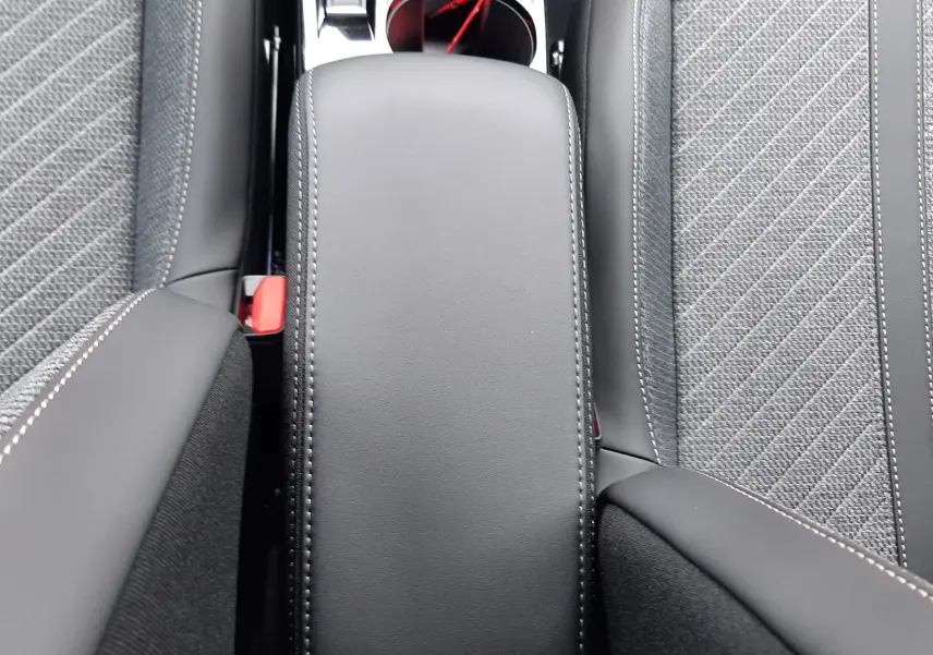 Gros plan sur l'accoudoir central noir et les sièges gris tissu avec surpiqûres blanches dans un Peugeot 2008 hybride 2025.
