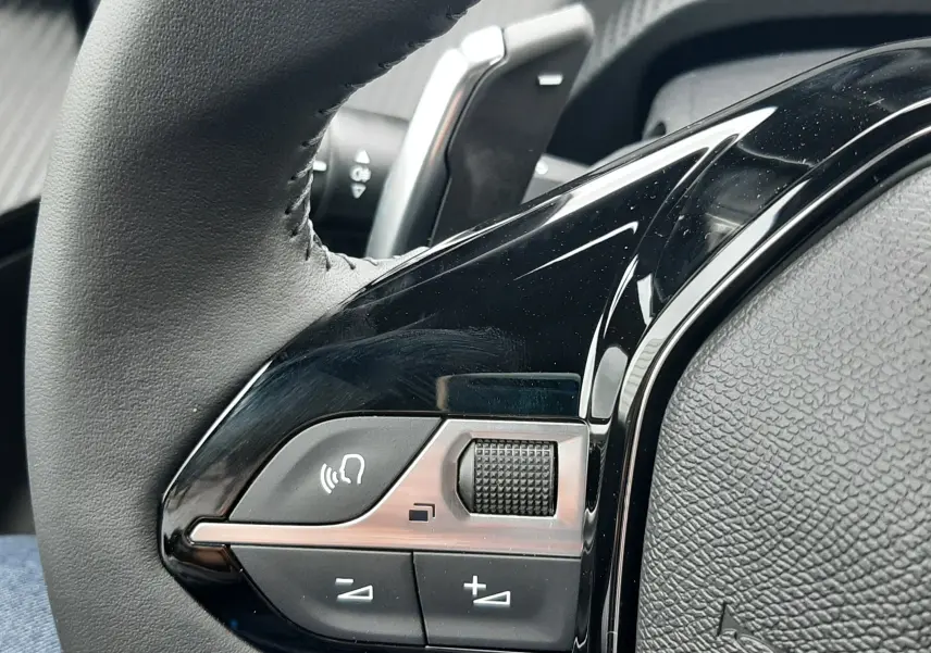 Gros plan sur les commandes gauche du volant en cuir noir du Peugeot 2008 gris Artense, avec molette et boutons de volume.