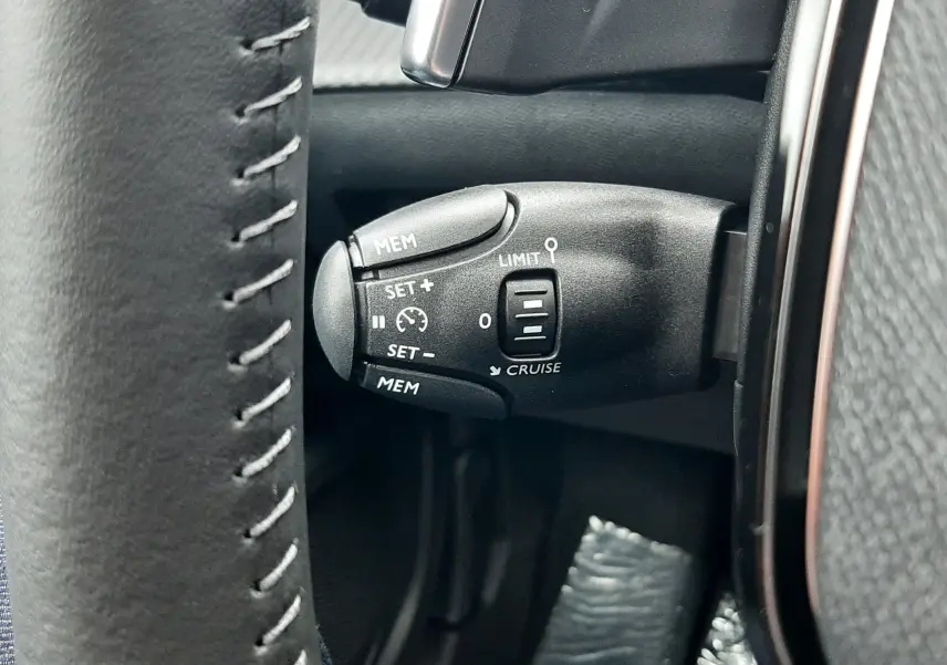 Gros plan sur la commande de régulateur de vitesse à gauche du volant cuir gris du Peugeot 2008 hybride 2025.
