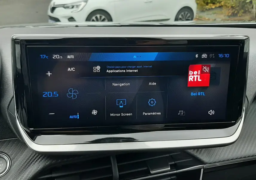 Écran tactile central du Peugeot 2008 2025 affichant le menu navigation et climatisation, avec une voiture blanche en arrière-plan.