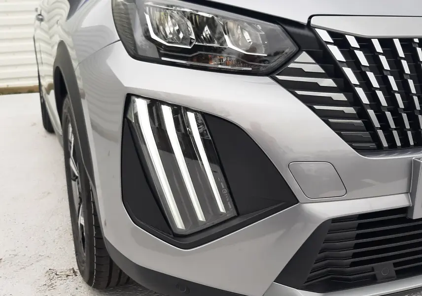 Gros plan sur l'avant droit du Peugeot 2008 gris Artense, mettant en valeur ses phares LED et la calandre distinctive.