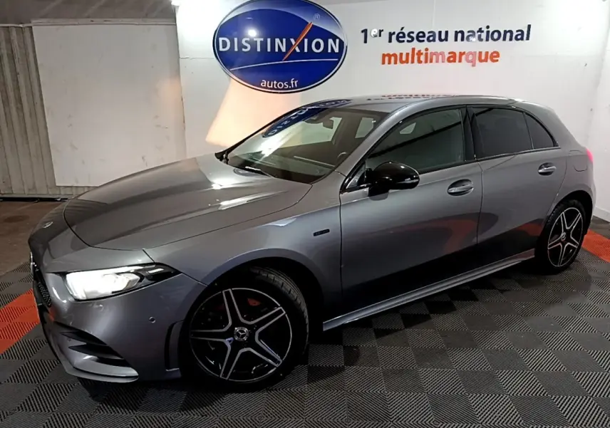 Vue 3/4 avant droit d'une Mercedes Classe A 250 e AMG Line gris foncé avec jantes alliage noires et phares LED allumés.
