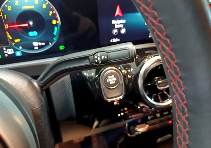 Vue rapprochée du volant cuir avec surpiqûres rouges et levier de vitesses sur tableau de bord noir brillant d'une Mercedes Classe A.