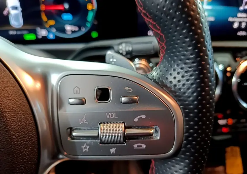 Gros plan sur le volant cuir et alu avec commandes multifonctions de la Mercedes Classe A 250 e AMG Line gris foncé.