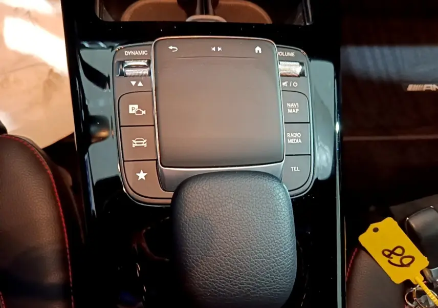 Gros plan sur la console centrale noire brillante de la Mercedes Classe A 250 e AMG Line avec pavé tactile et accoudoir cuir.