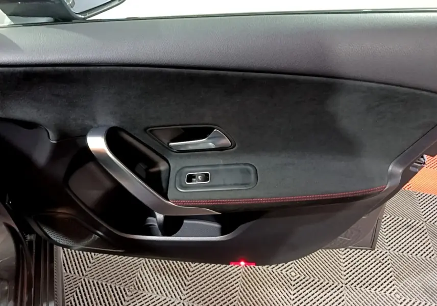 Vue intérieure du panneau de porte côté gauche de la Mercedes Classe A 250 e AMG Line gris foncé avec surpiqûres rouges et poignée alu.