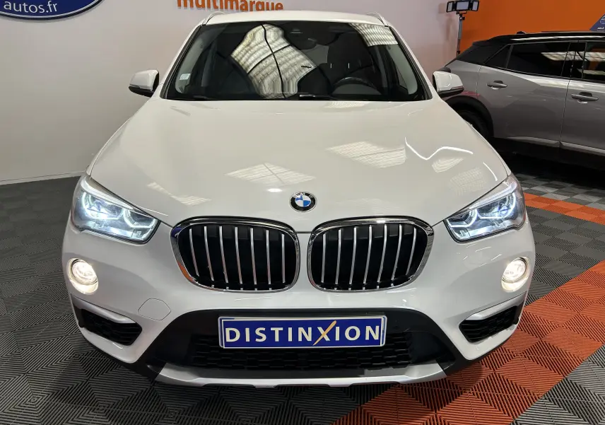 Vue frontale d’un BMW X1 blanc avec phares LED allumés et calandre double haricot caractéristique.