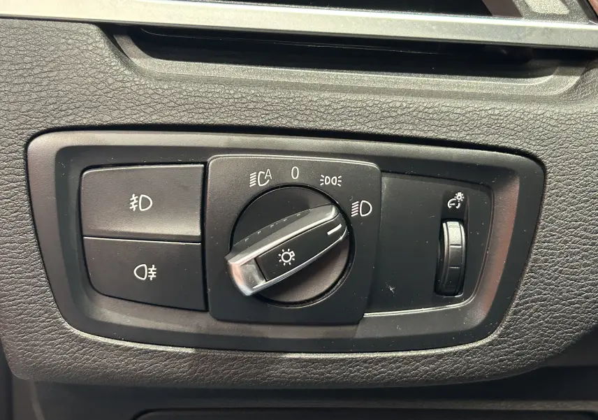 Gros plan sur le panneau de commande des phares intérieurs d'une BMW X1 blanche de 2018, avec molette centrale et réglage d'intensité.
