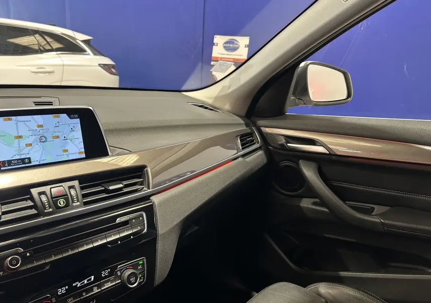 Vue intérieure côté passager du tableau de bord et de la portière d'une BMW X1 blanche, avec écran de navigation allumé.